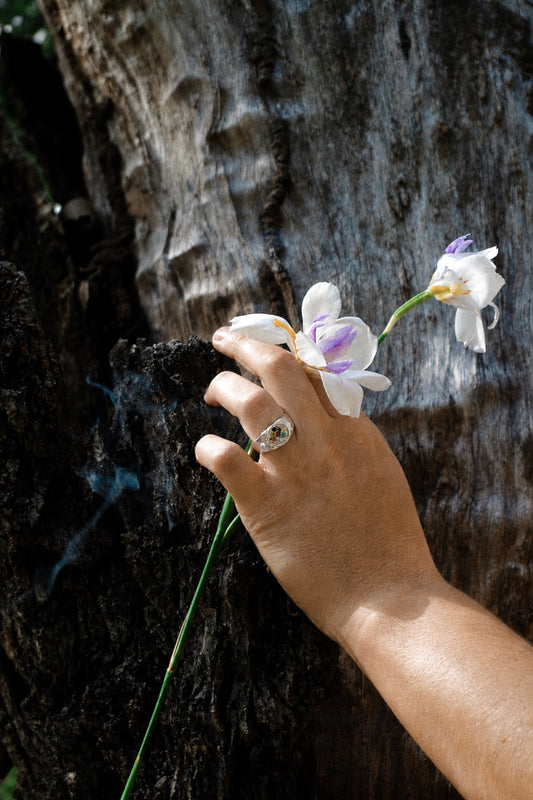 Ananta recycled sterling silver gemstone ring worn on a hand holding white flowers against tree bark